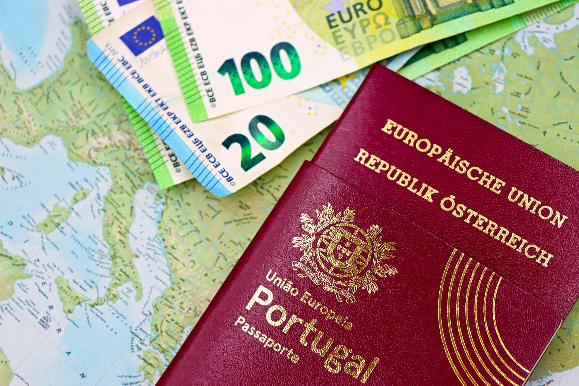 A Portuguese passport lies next to an Austrian passport on top of a map with euro banknotes.