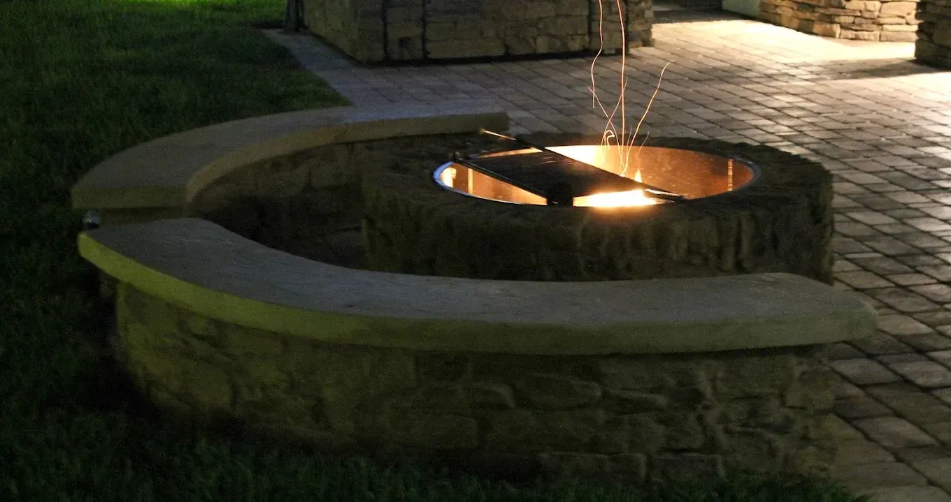Fire pit with surrounding stone seating at night. Sparks fly upwards.