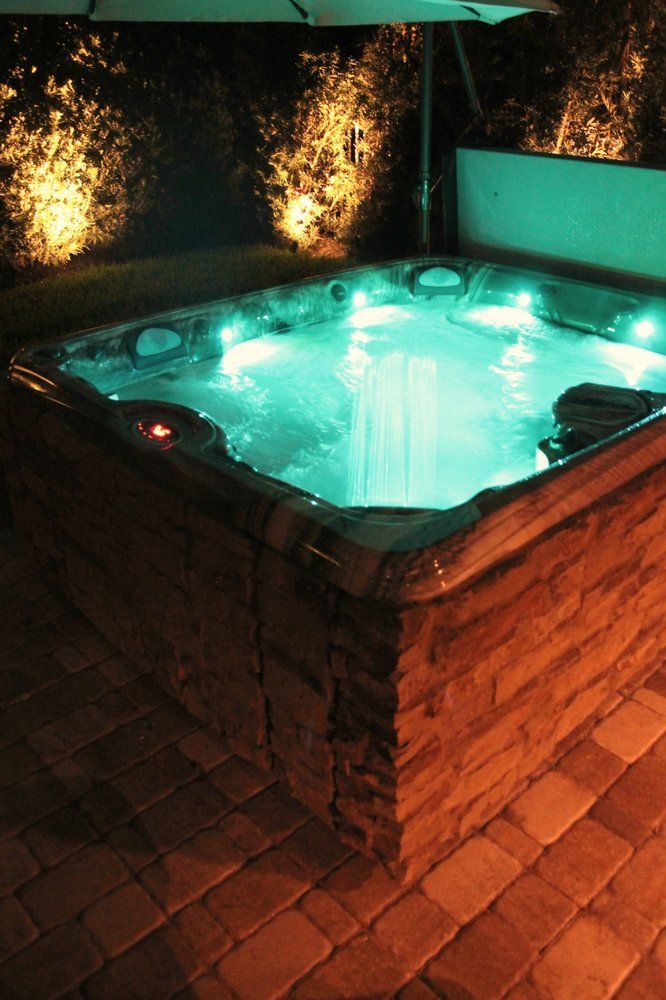 Lit-up hot tub with turquoise water at night, surrounded by brick and patio stones.