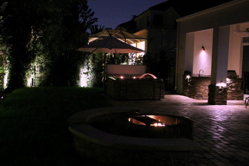 Nighttime backyard scene with lit fire pit, patio, seating, and house.