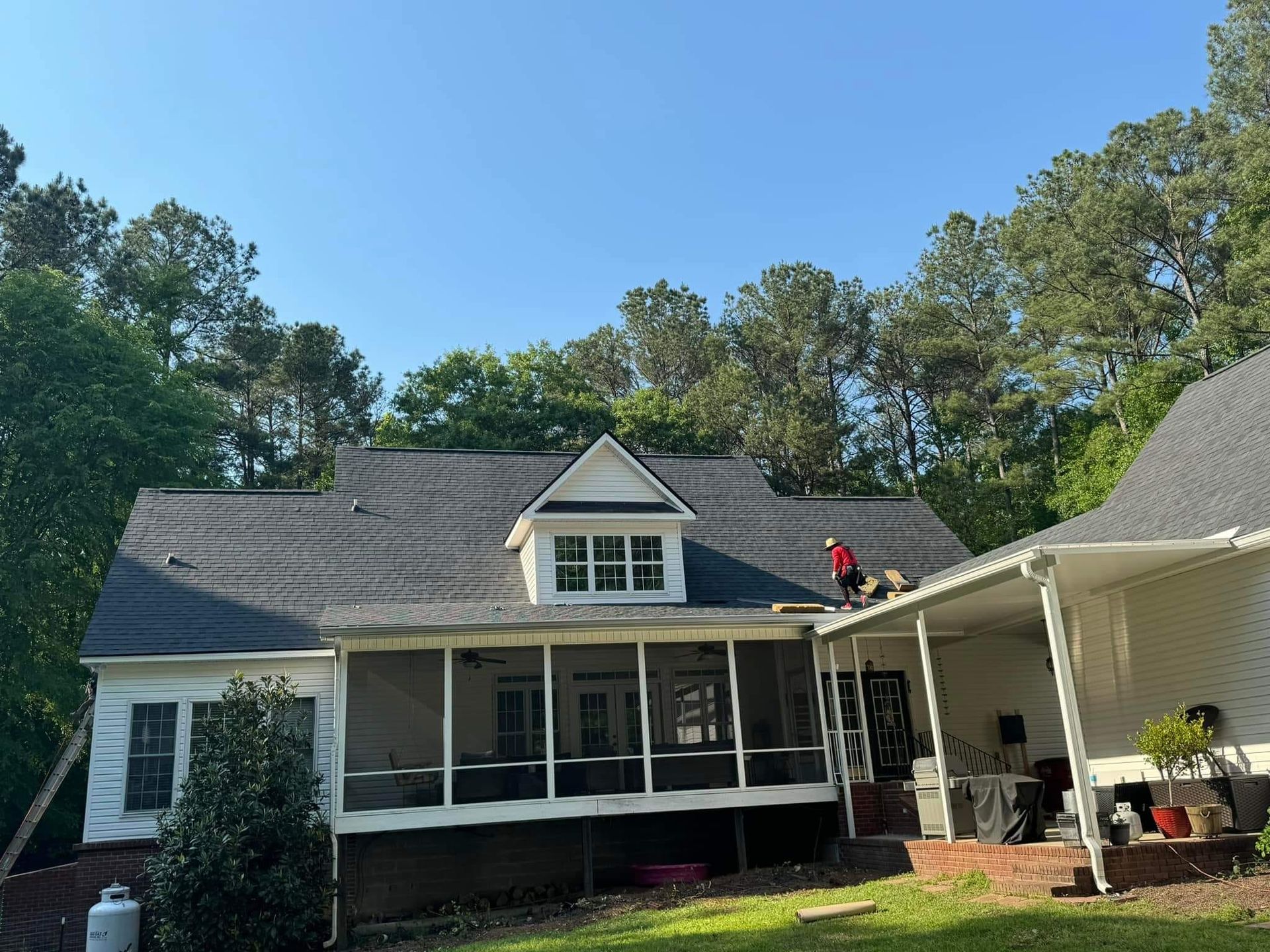 A man is working on the roof of a house with a screened in porch.
