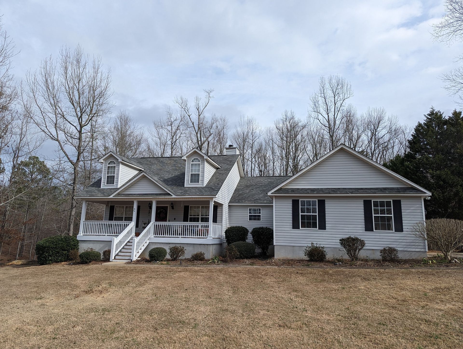 A large white house with a large porch in the middle of a field.