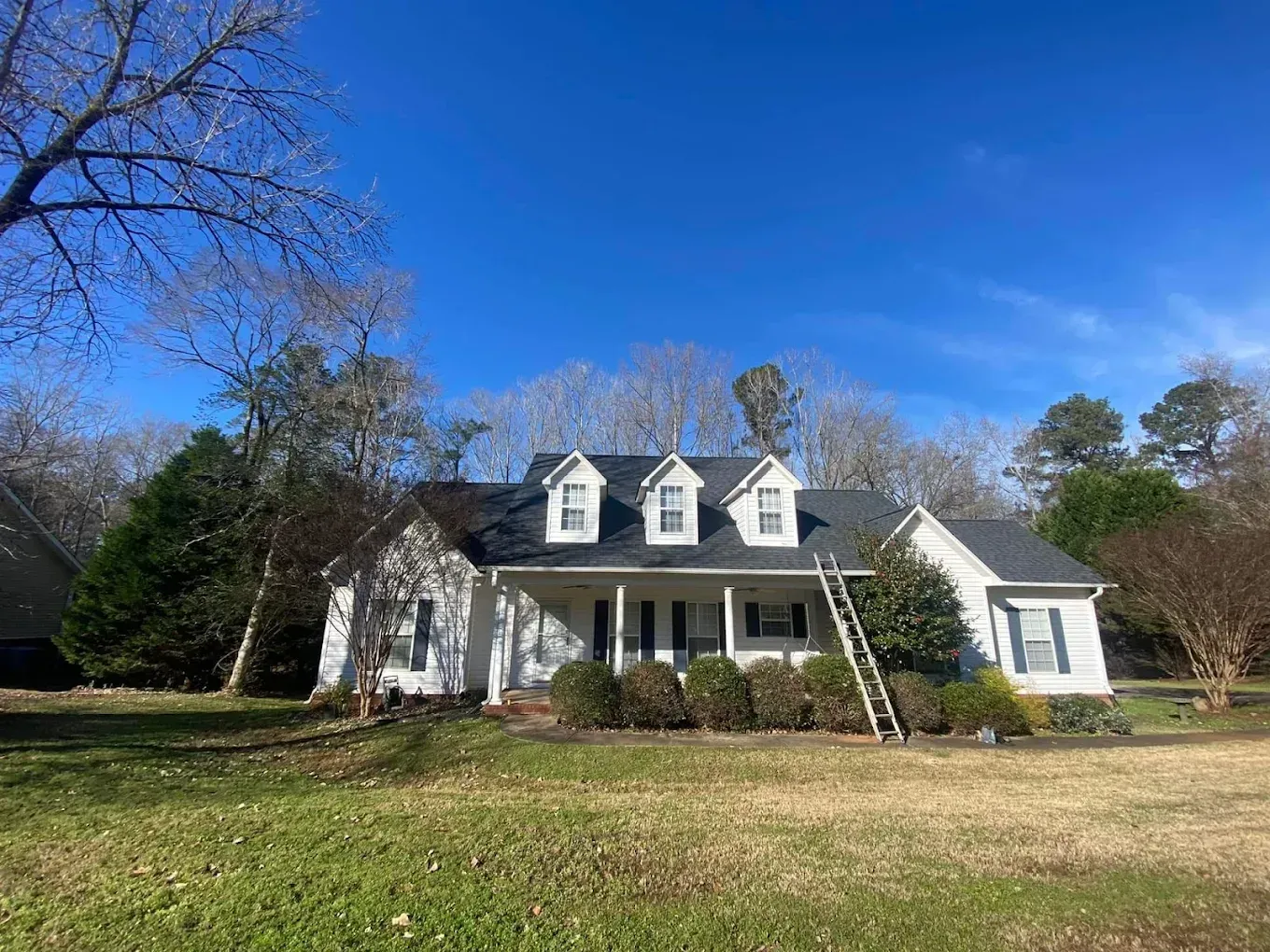 A large white house with a black roof and a ladder in front of it.