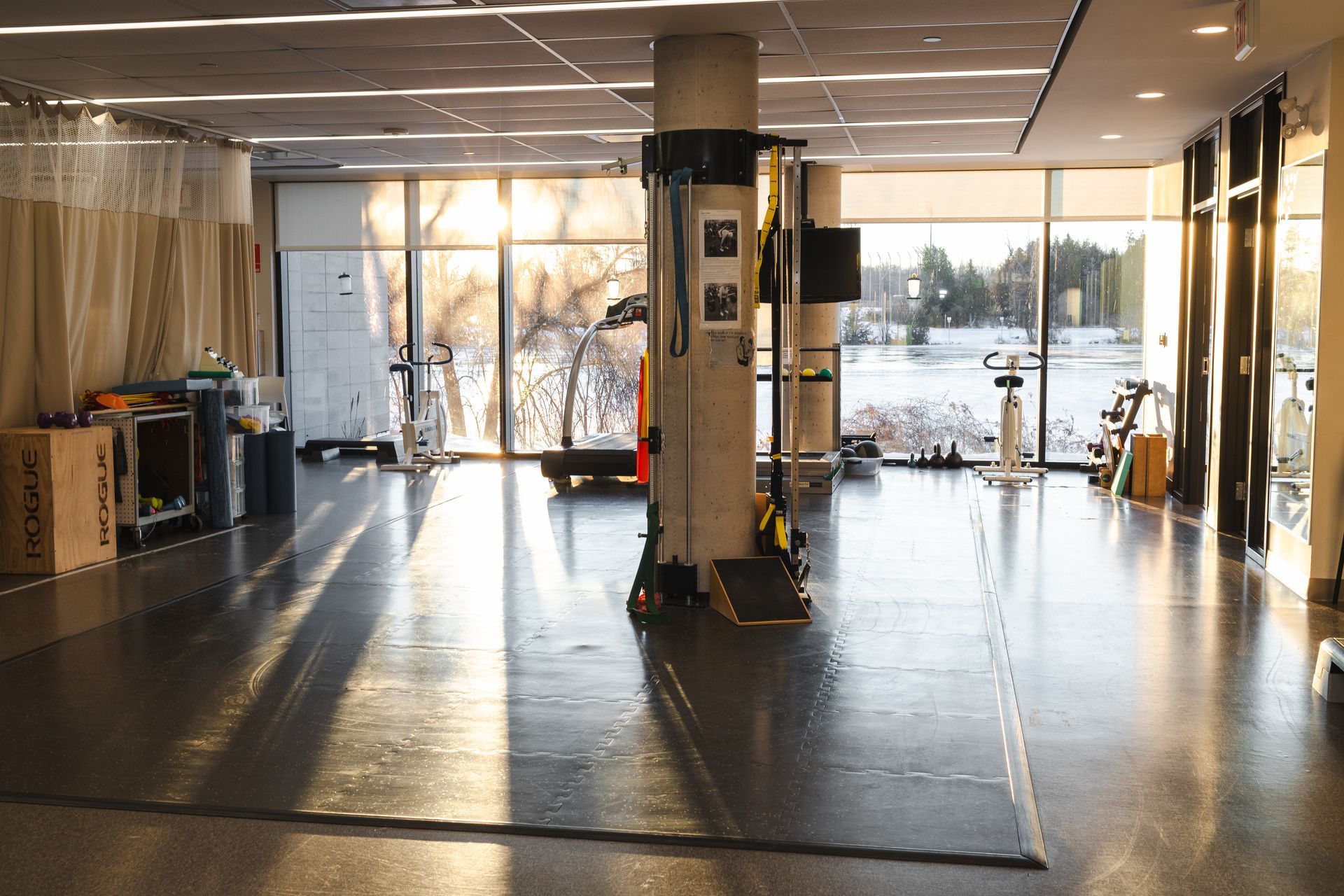 Gym with large windows overlooking a snowy landscape. Sunlight streams across a gray floor.