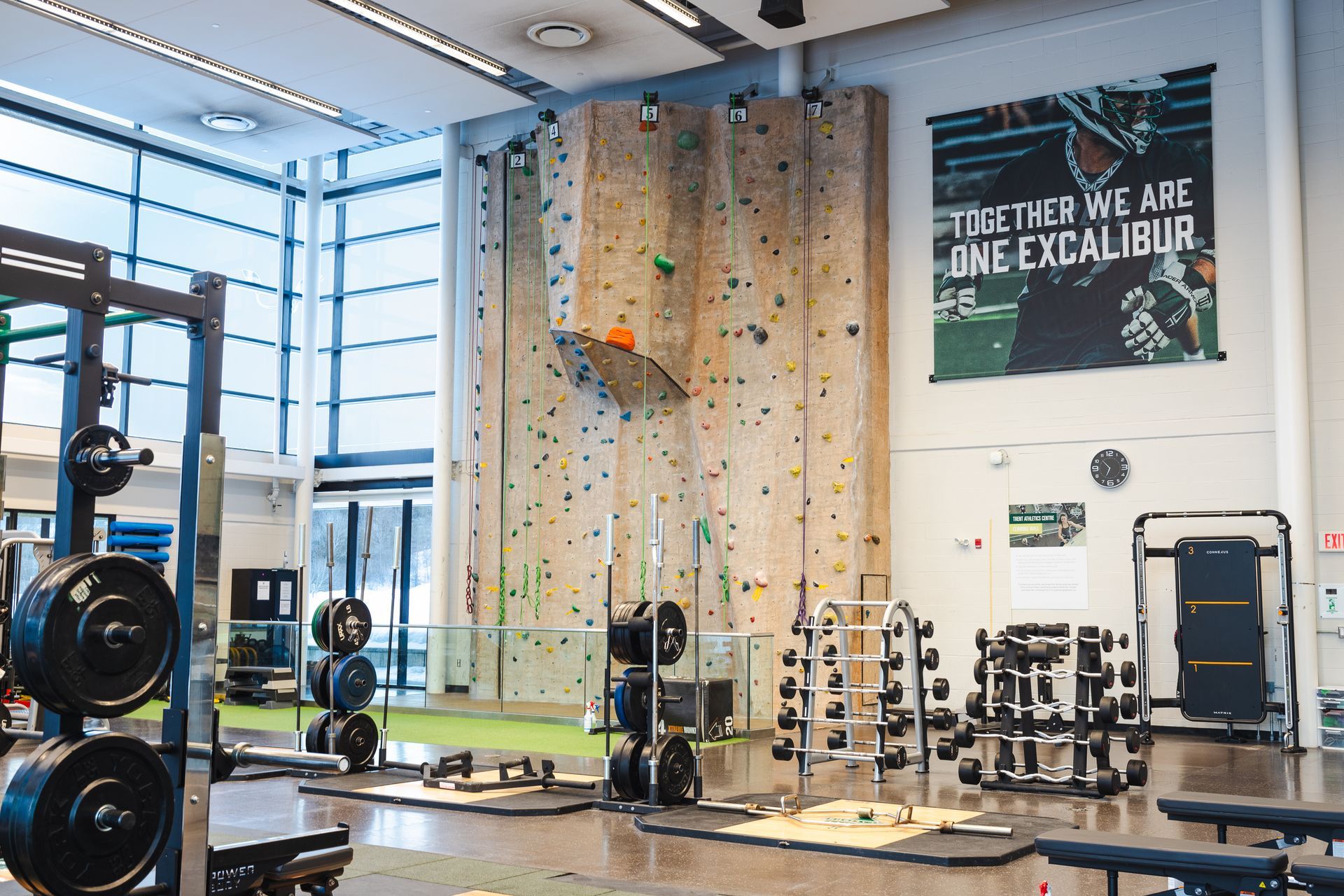 Gym with weight racks, climbing wall, and motivational banner.