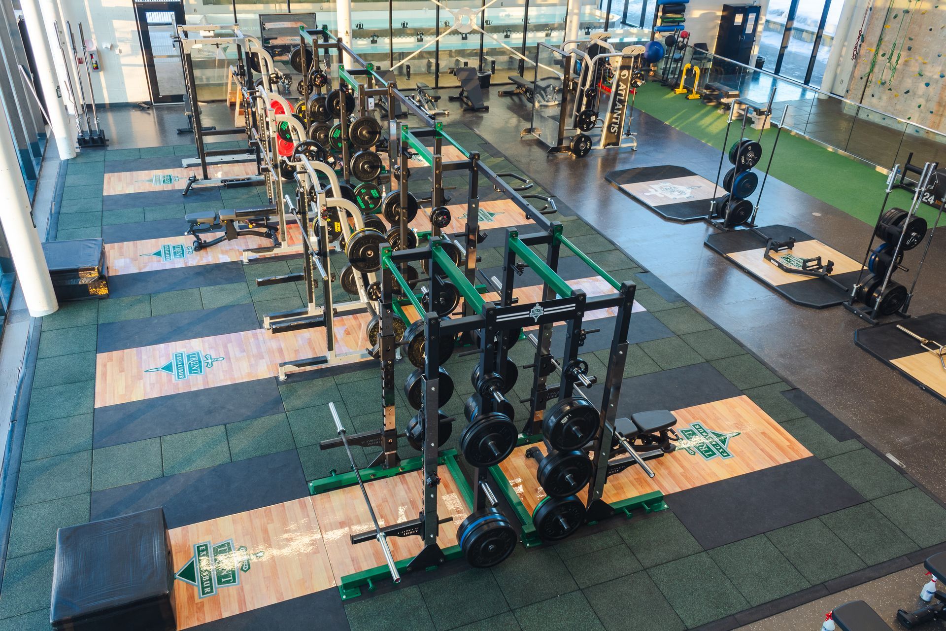 Gym interior with weight racks, equipment, and rubber flooring; green and black color scheme.