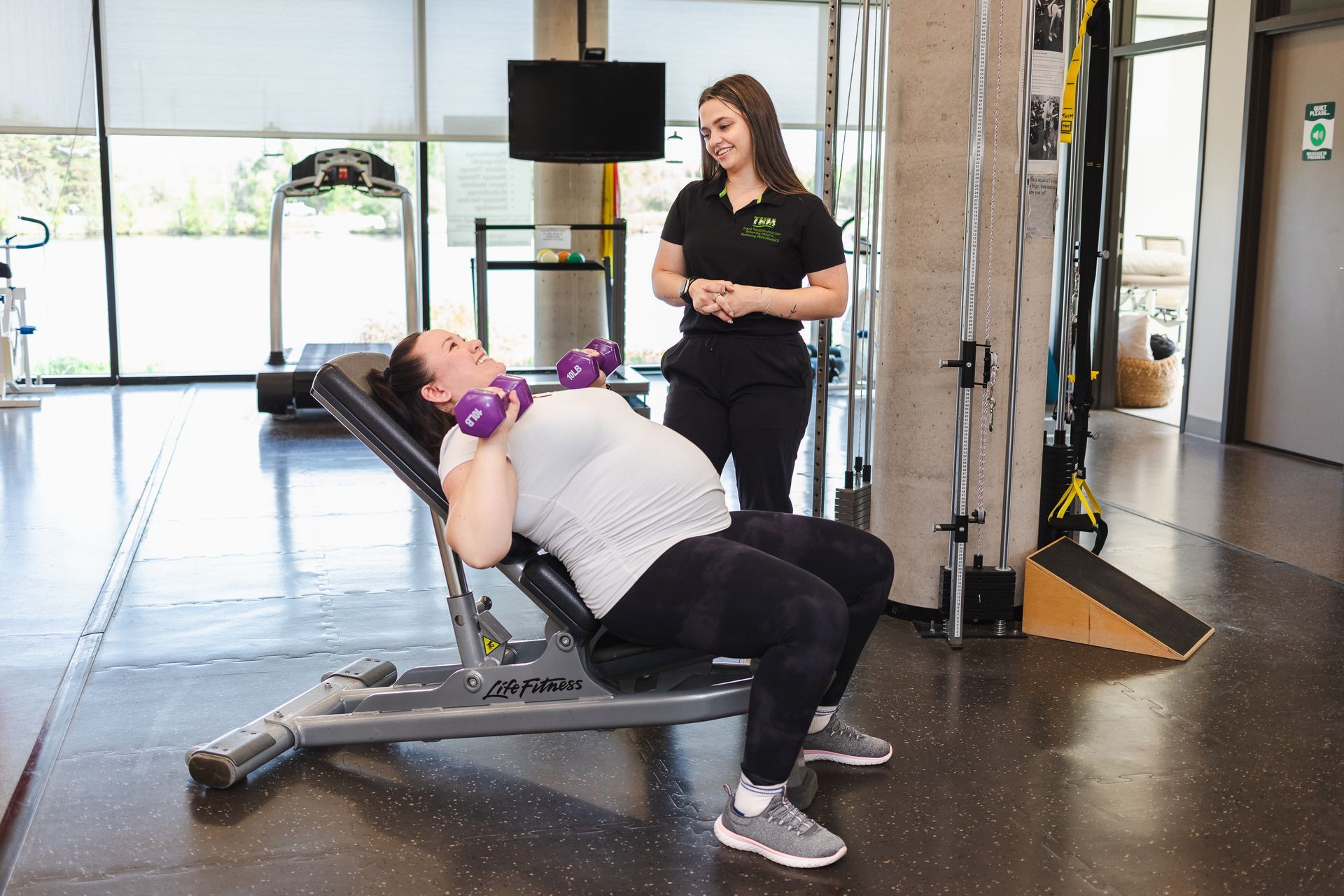 Pregnant woman doing bridge exercise with trainer in physiotherapy clinic.