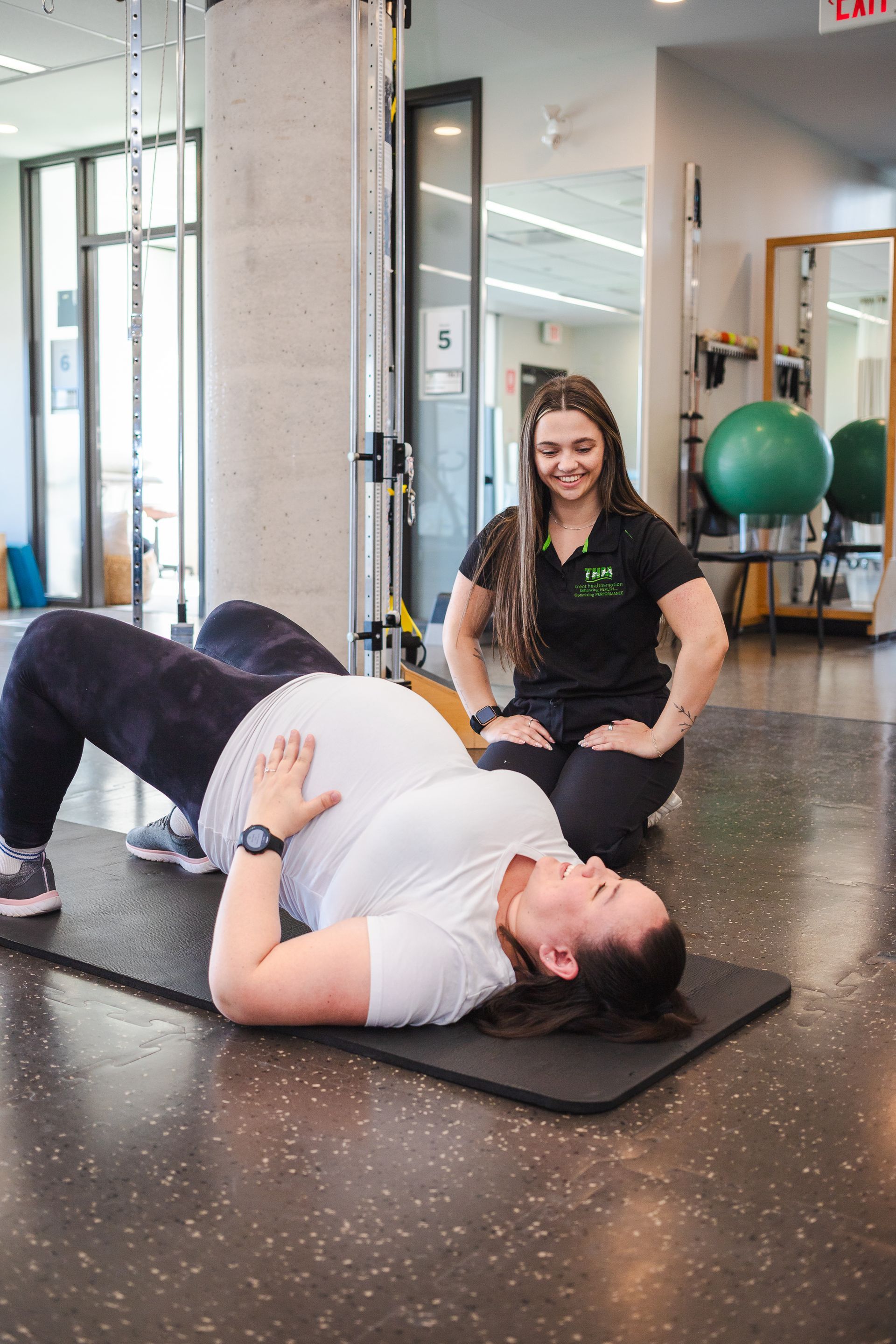 Pregnant woman doing bridge exercise with trainer in physiotherapy clinic.