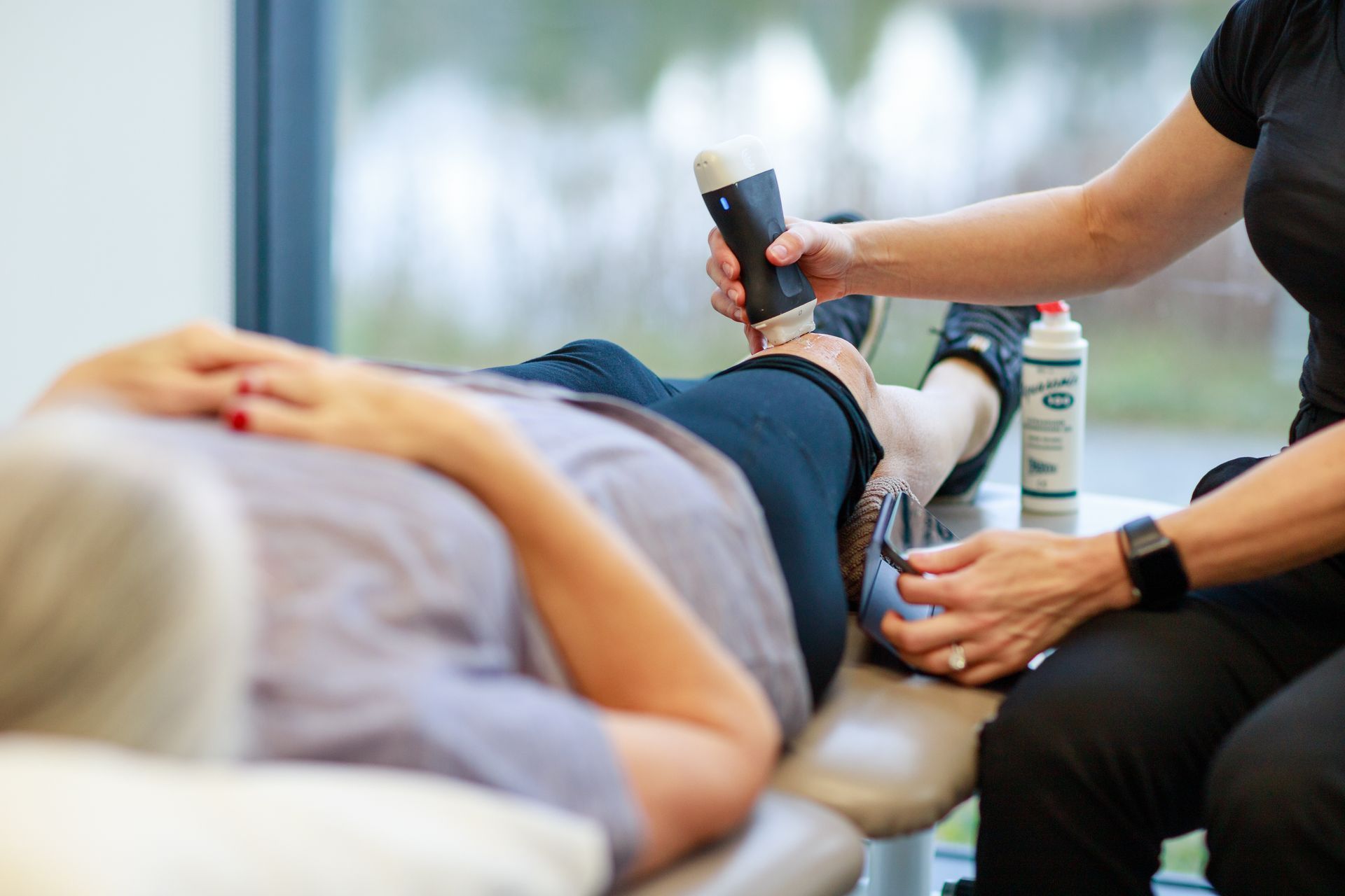 Therapist using ultrasound device on patient's ankle. White, professional setting.