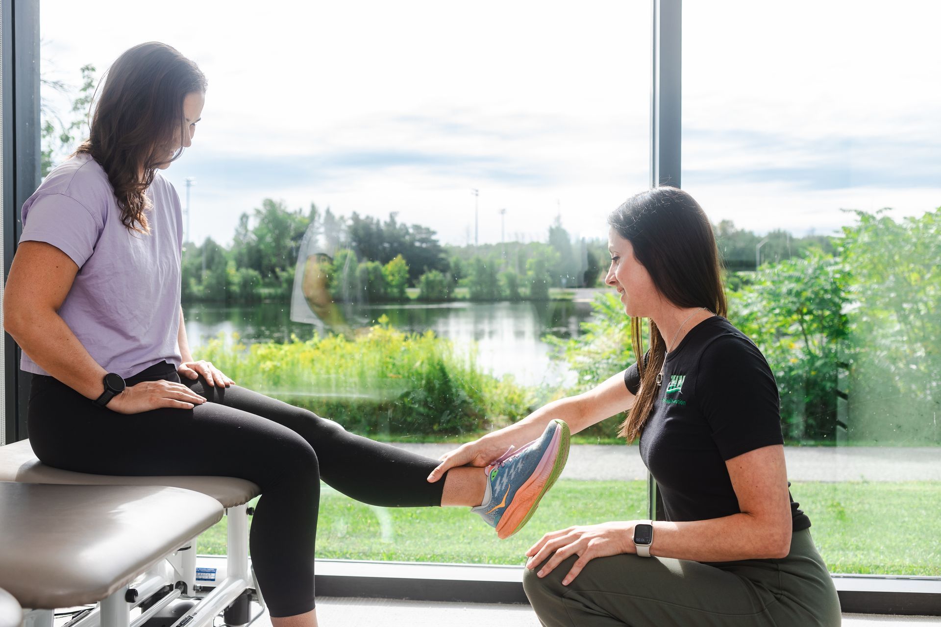 Woman getting physical therapy from a therapist, near a large window.