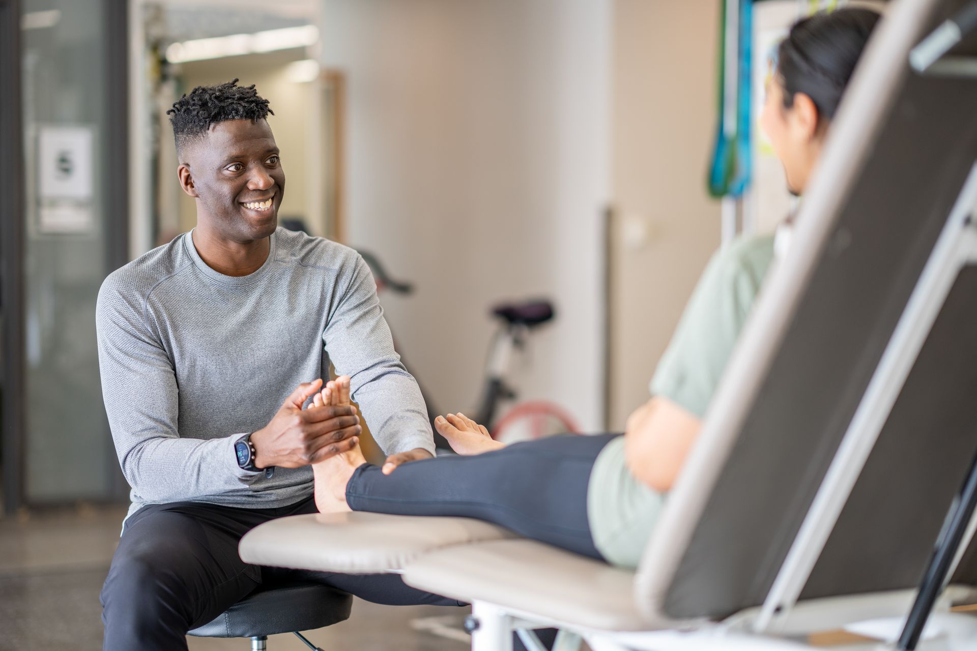 Physical therapist treating a patient's foot. Man smiles as he holds the woman's foot. Therapy room setting.