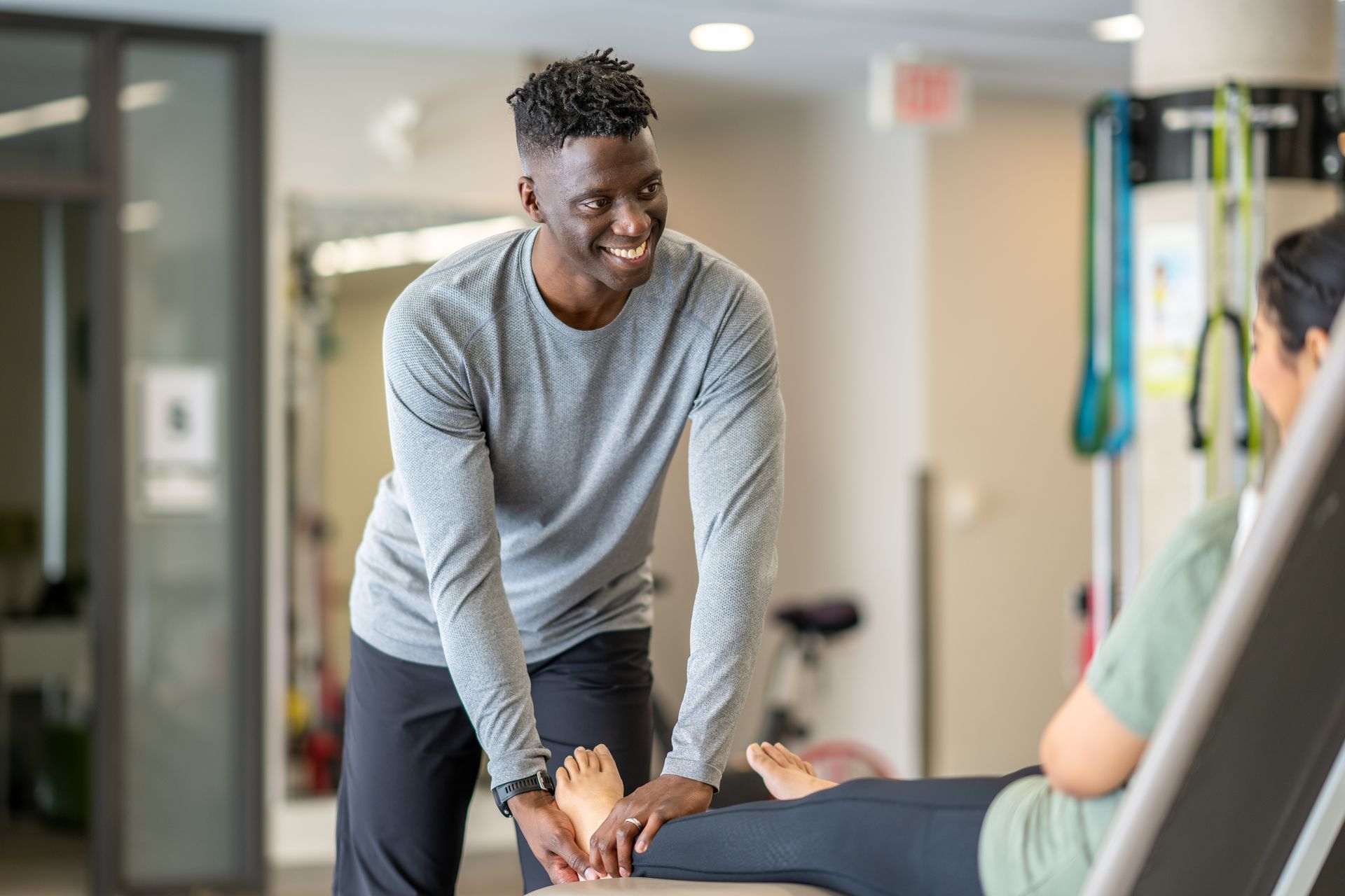 A man is helping a woman stretch her leg in a gym.