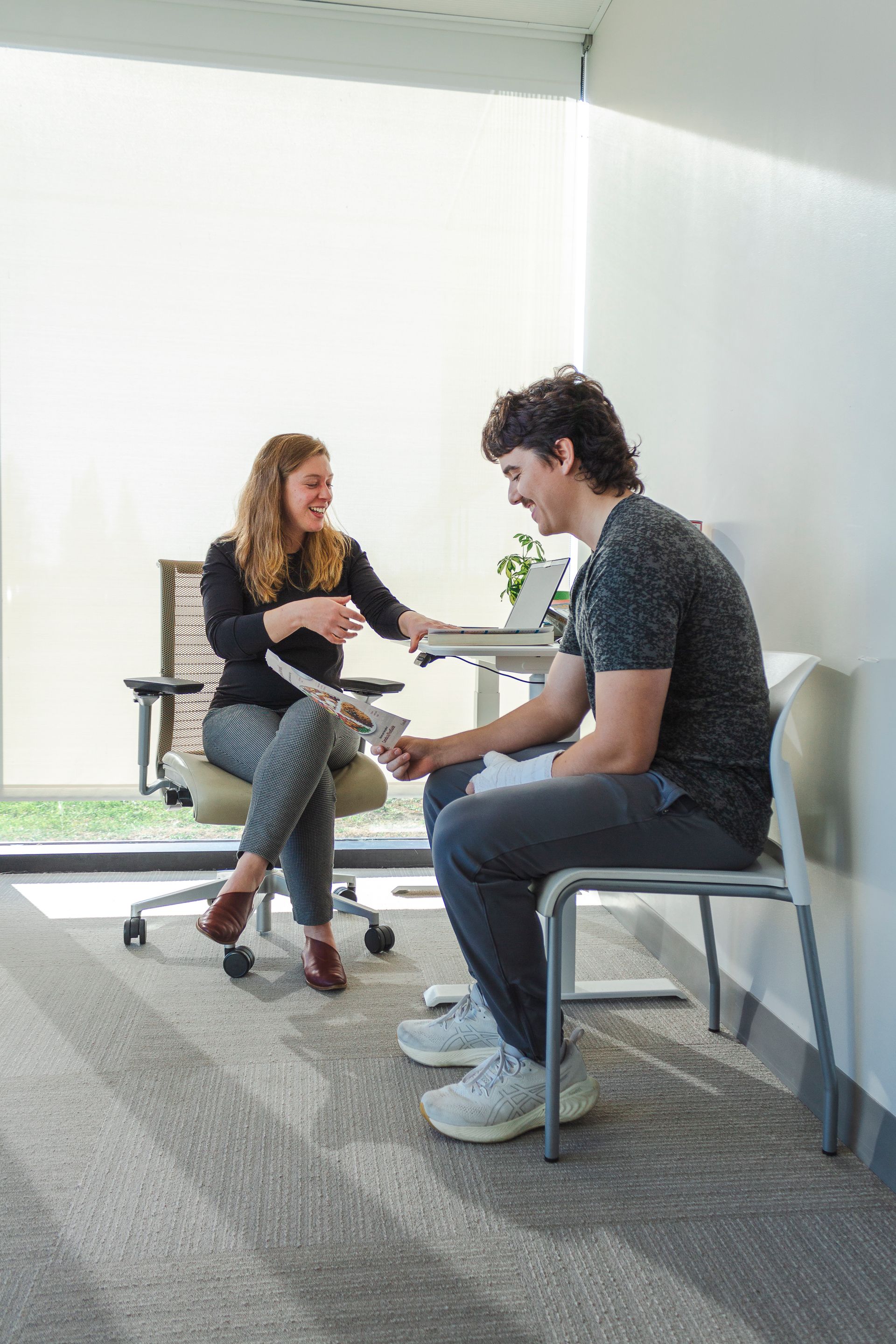 A man and a woman are sitting in chairs in a room talking to each other.