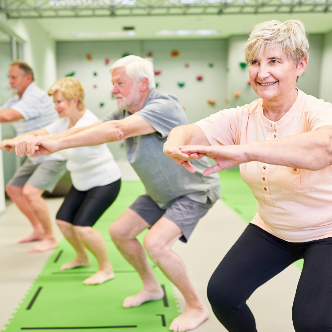 A group of people are squatting on a green mat in a gym.