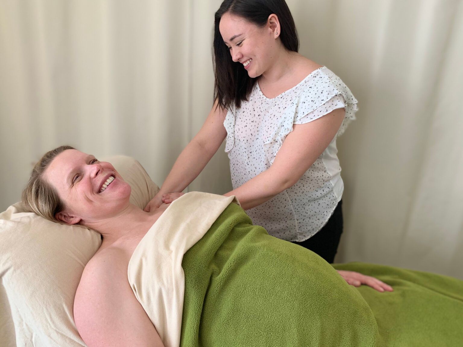 A woman is giving a massage to a woman laying on a bed.