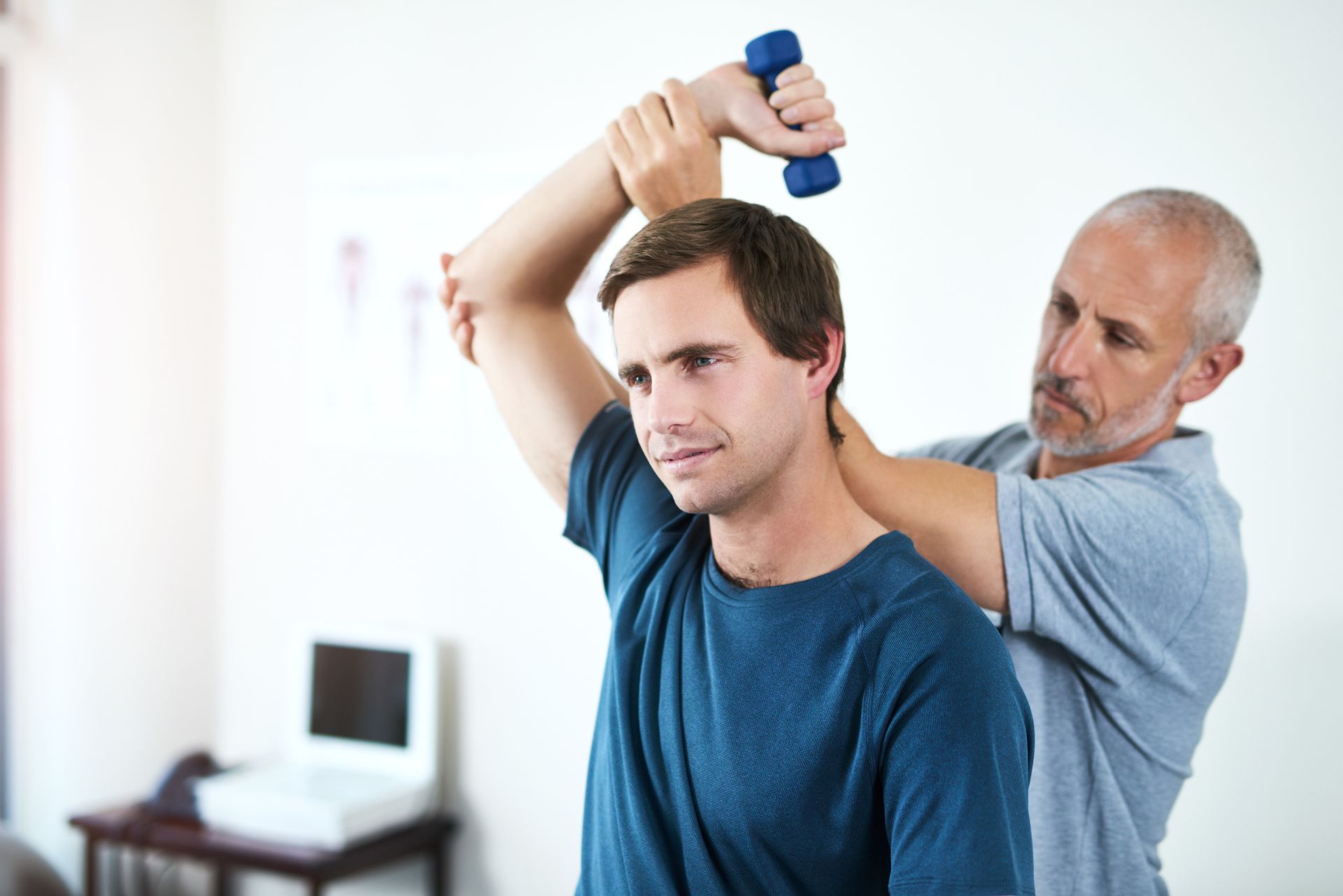 Man receiving physical therapy with a dumbbell, indoors.