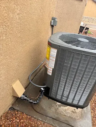 Outdoor HVAC unit beside a stucco wall with a disconnected chain and cardboard near the base