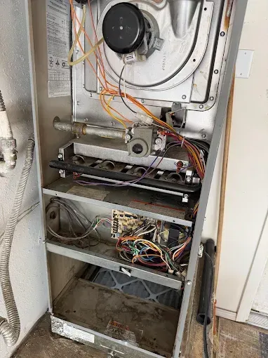 Open furnace cabinet with exposed wiring, fan, and dusty interior panels.