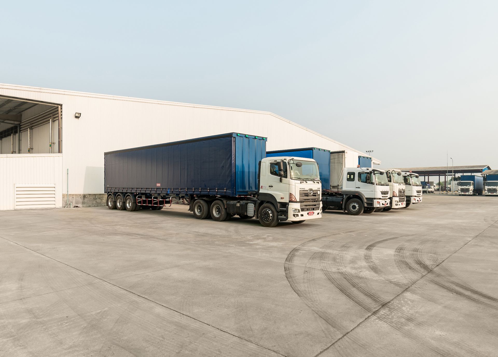 A row of trucks are parked in a parking lot in front of a building.