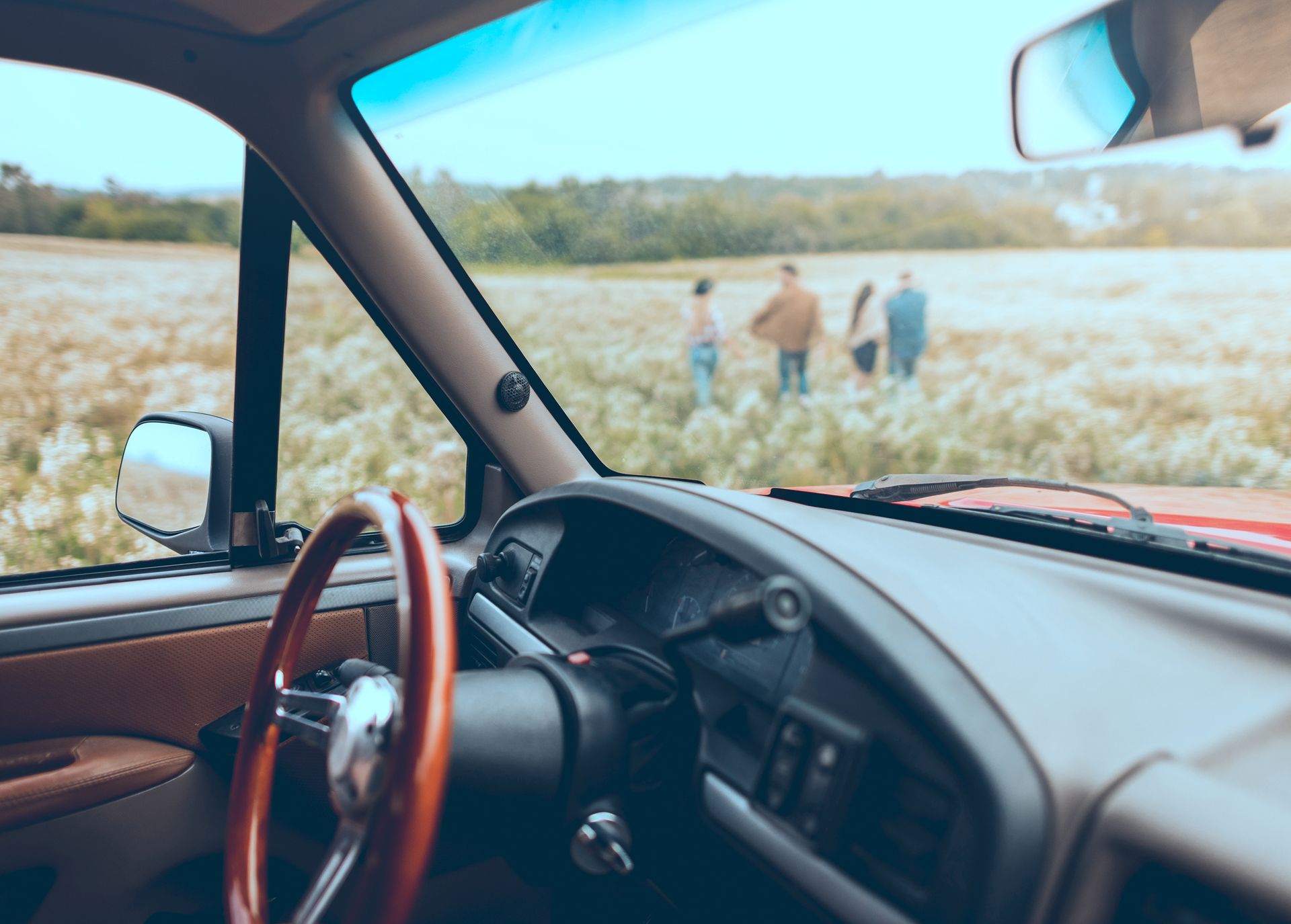 The inside of a car with a wooden steering wheel and a group of people standing in a field.