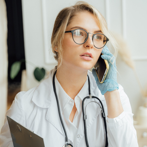 a female doctor wearing glasses and a stethoscope is talking on a cell phone .