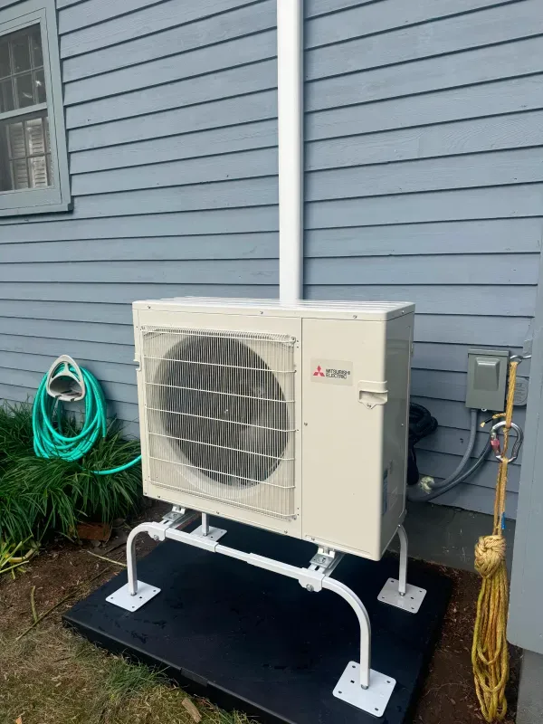 Mitsubishi heat pump unit outside a house, with a white support structure and venting.