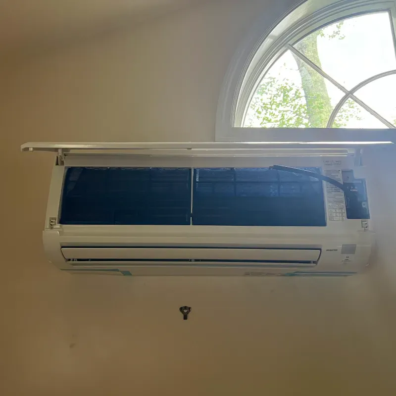 White air conditioning unit mounted on a beige wall under a rounded window.