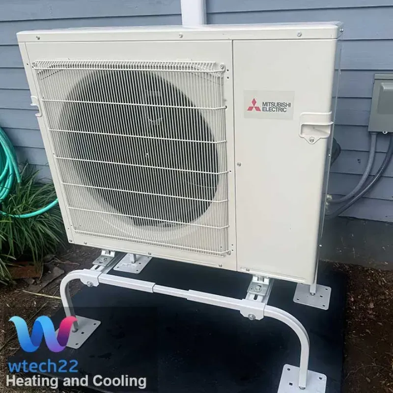 Mitsubishi Electric heat pump unit on white metal stand, next to a building.