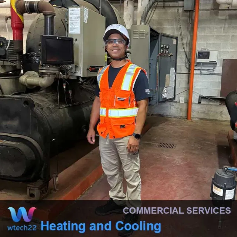 A person in safety gear stands near commercial heating/cooling equipment.