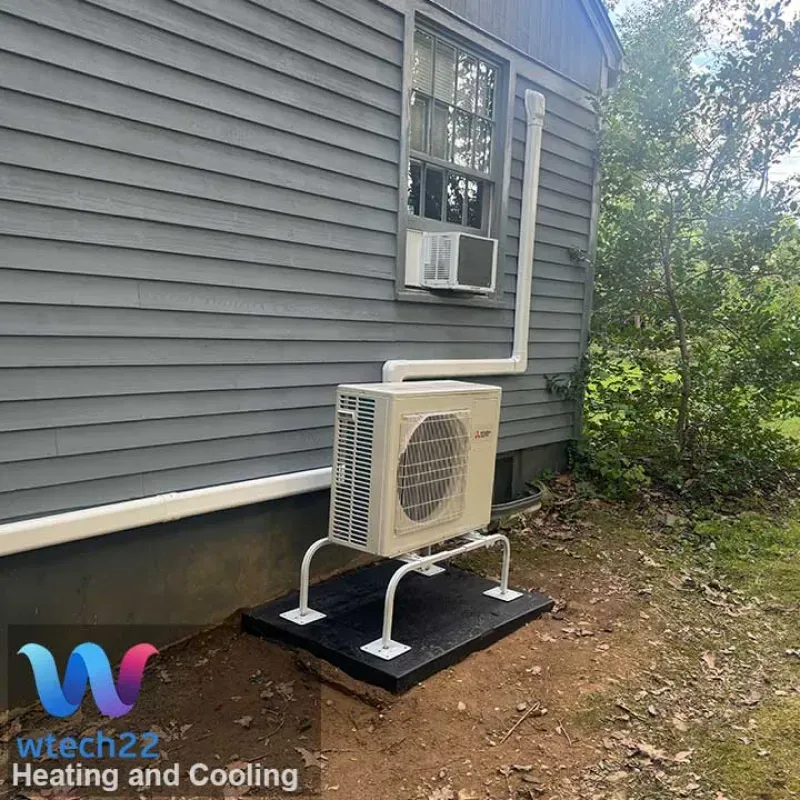 An outdoor HVAC unit on a platform, attached to a house with white piping and an above window unit.