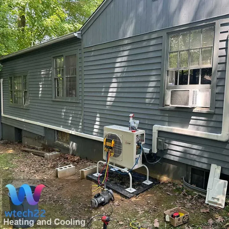 An air conditioning unit is installed outside a gray house with a window AC unit.