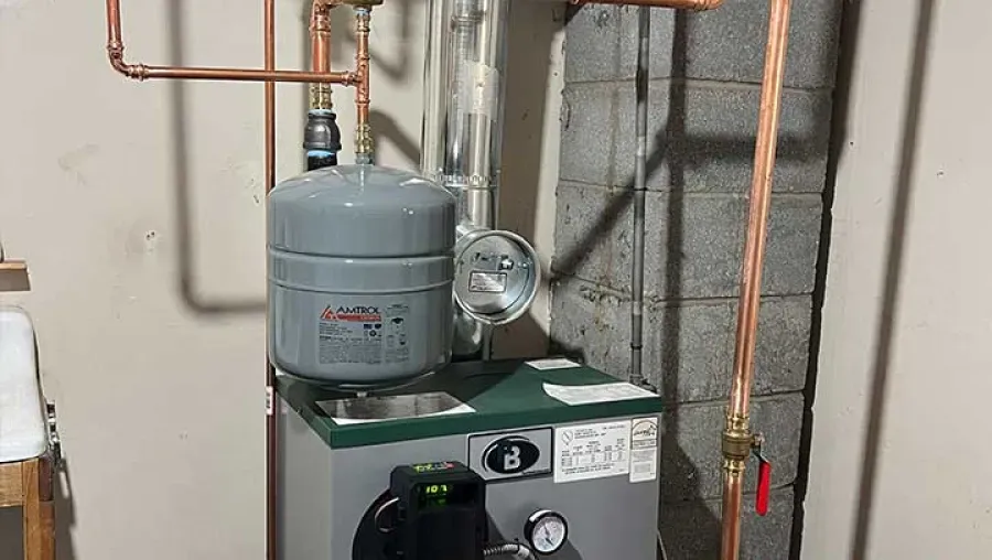 A boiler system with copper pipes, a gray expansion tank, and a pressure gauge, set in a utility room.