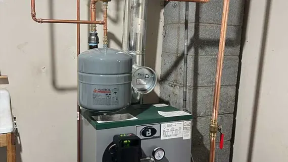 A boiler system with copper pipes, a gray expansion tank, and a pressure gauge, set in a utility room.
