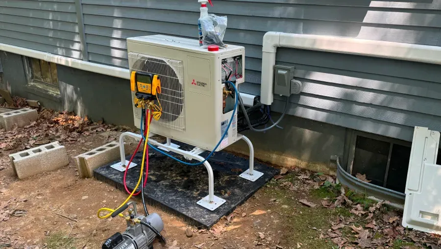 An air conditioner unit outside a house is being serviced with gauges and vacuum pump.