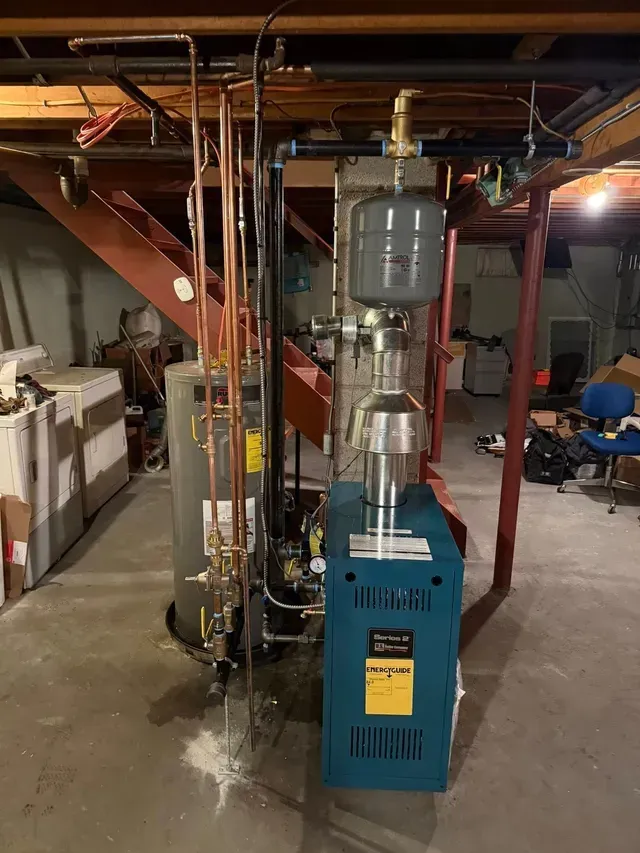 Basement with boiler, hot water tank, expansion tank, copper pipes, and exposed ductwork.