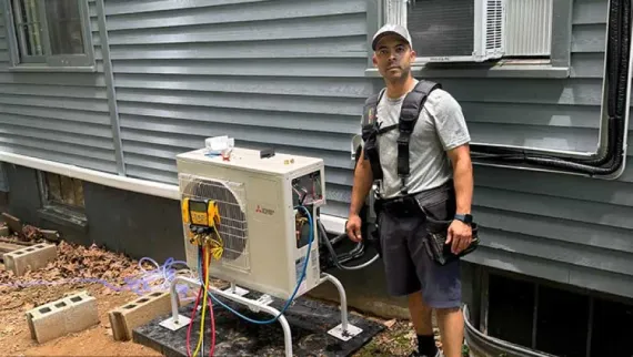 HVAC technician next to air conditioning unit, outdoor setting, gauges attached.
