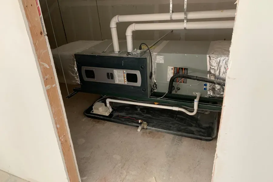 HVAC unit in a utility room, with white pipes and black base, viewed from doorway.