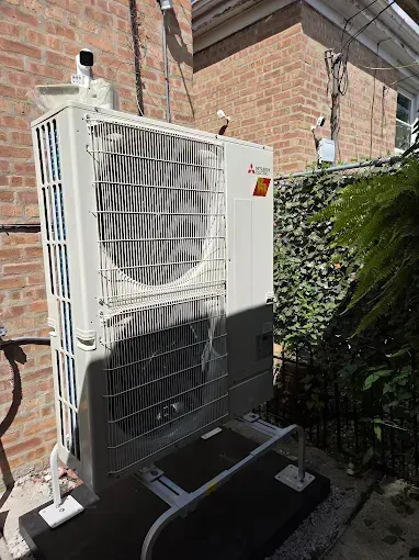Mitsubishi HVAC unit against a brick wall, with protective cage and black base.