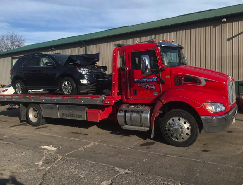 Red tow truck carrying a heavily damaged black SUV | Downtown Auto Clinic