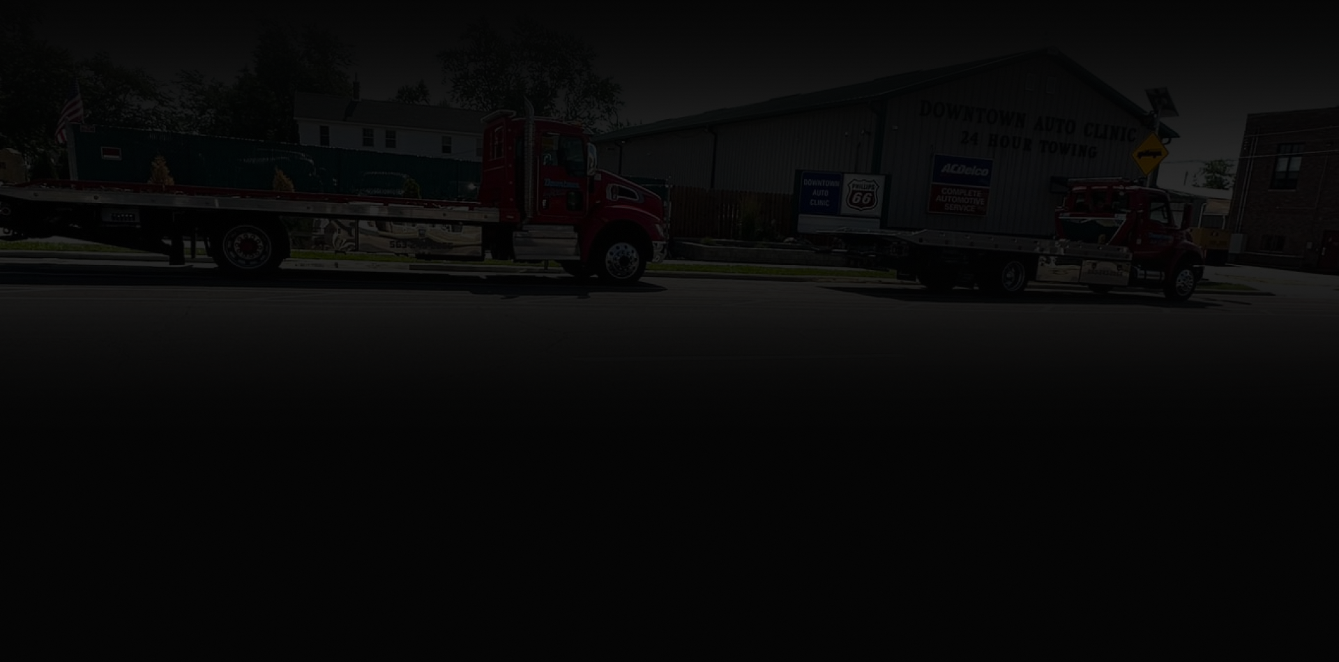 Two red flatbed trucks parked outside a building | Downtown Auto Clinic