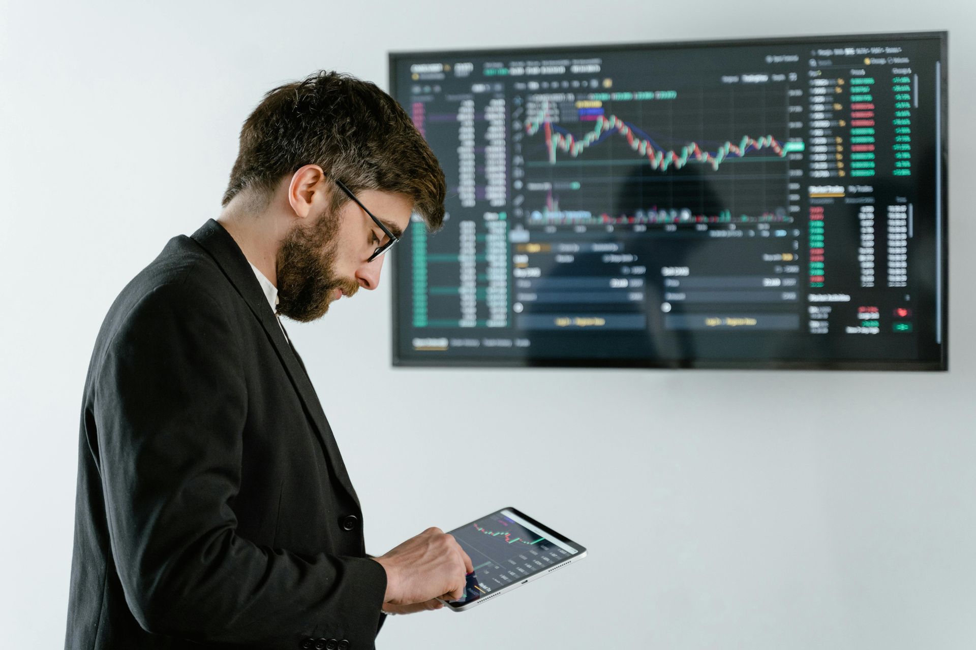 A man in a suit is looking at a tablet in front of a large screen.