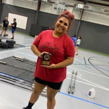 A woman in a red shirt is holding a trophy in a gym