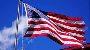 An american flag is waving in the wind against a blue sky