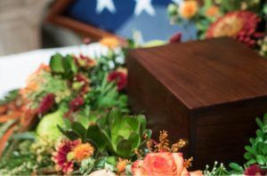 A wooden box is surrounded by flowers and a flag.