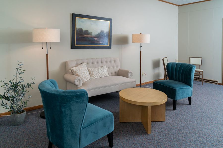 A living room with a couch , chairs , a table and a painting on the wall.