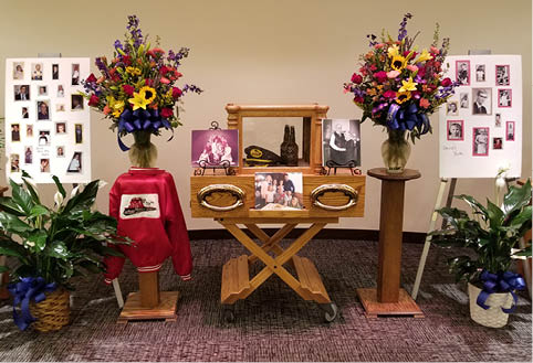 A display of flowers , pictures , and a hat on a table in a room.