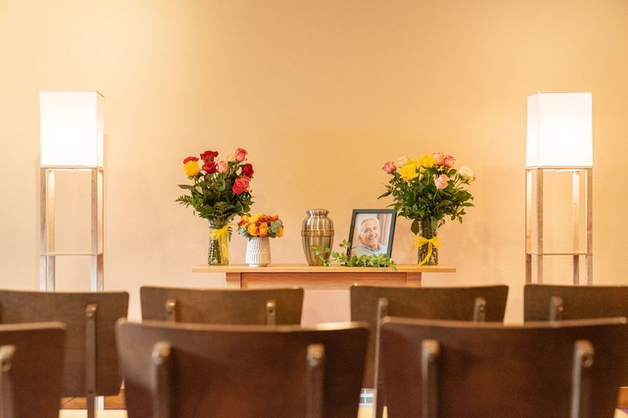 A row of chairs in front of a table with flowers and a picture on it.