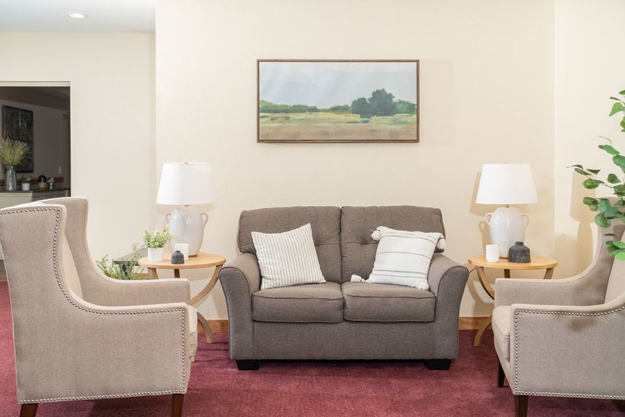A living room with a couch , chairs , lamps and a painting on the wall.