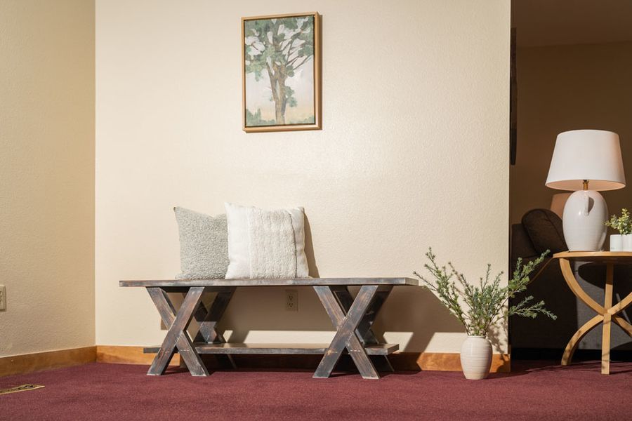 A living room with a bench and a lamp and a picture on the wall.