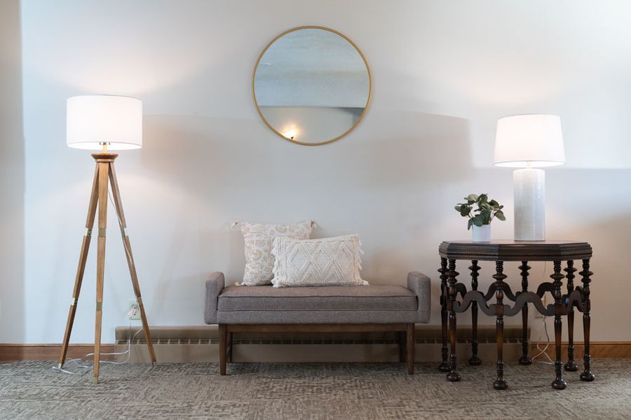 A living room with a bench , two lamps , a table and a mirror.